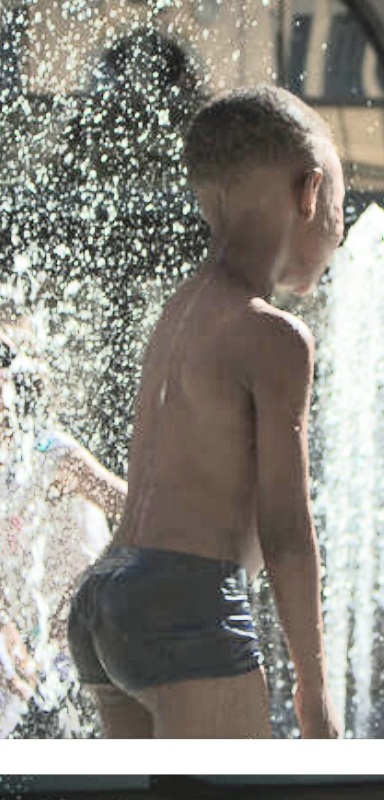 Black boy playing at water park fountain